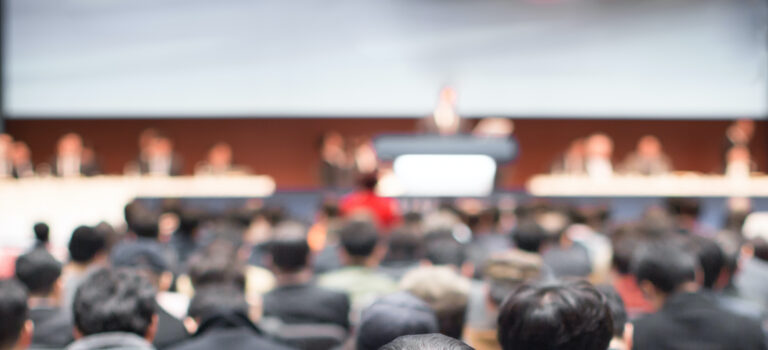 Blurred conference with panel speakers on stage during debate. Presenters at corporate seminar talking to audience.  Defocused business leadership CEO lecture. Executive board of directors